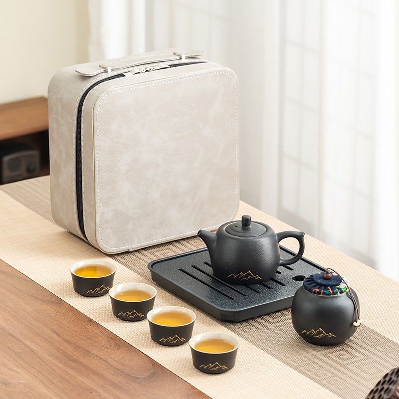 Four matching black cups arranged with the mountain-motif teapot, covered tea jar, slotted tray and cream case