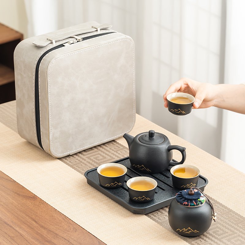One of four small black mountain-motif tea cups held above the tray beside the matching teapot and covered jar