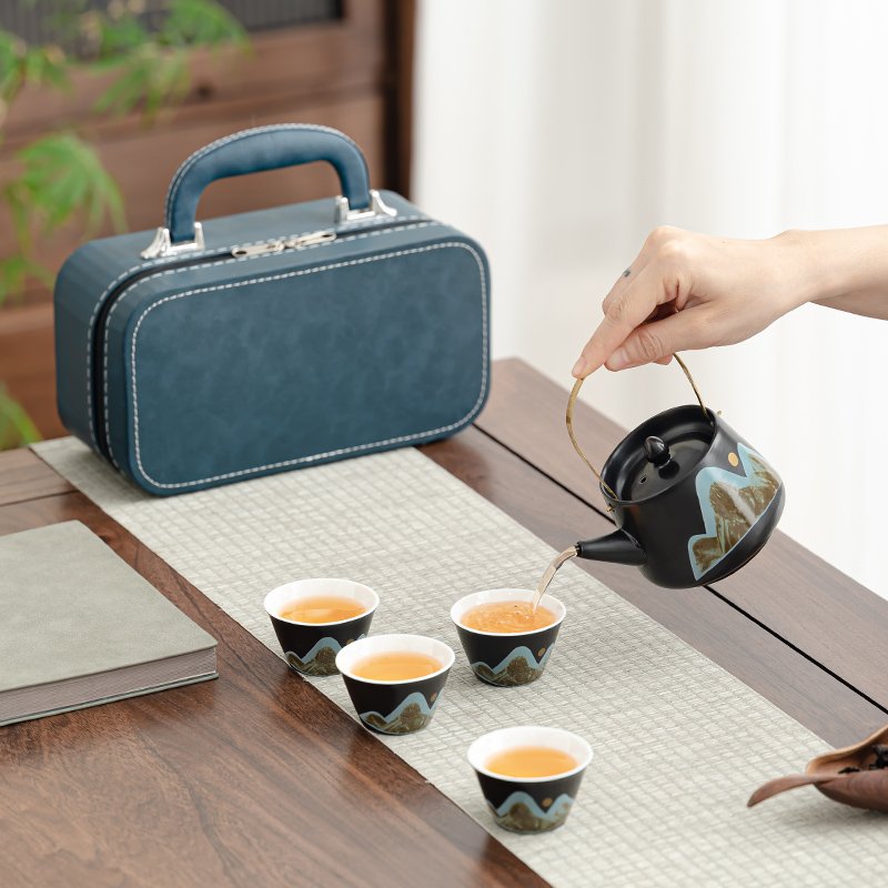 Overhead-handle ceramic teapot pouring tea into one of four matching mountain-landscape cups