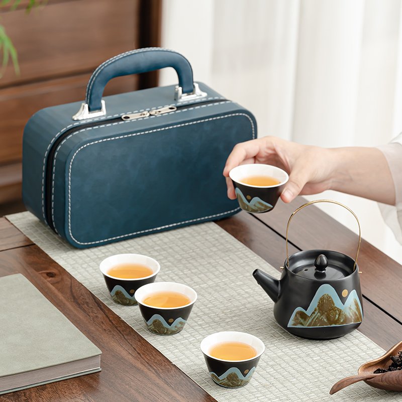 Mountain landscape on the dark teapot and four small cups beside their blue carrying case