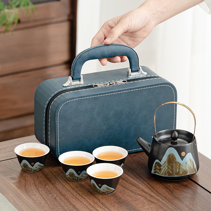 Blue zippered case held by its top handle with the mountain-landscape teapot and four cups arranged in front