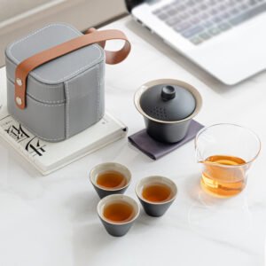 Black lidded brewing bowl, three tea cups, clear serving pitcher and gray carrying case