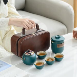 Teal tea set with four cups, a lidded brewing vessel, a covered jar and a brown carrying case held by its handle.