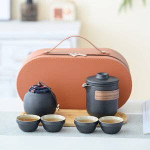 Black travel tea set with lidded brewer, four cups, covered tea jar, oval tray and orange-brown case