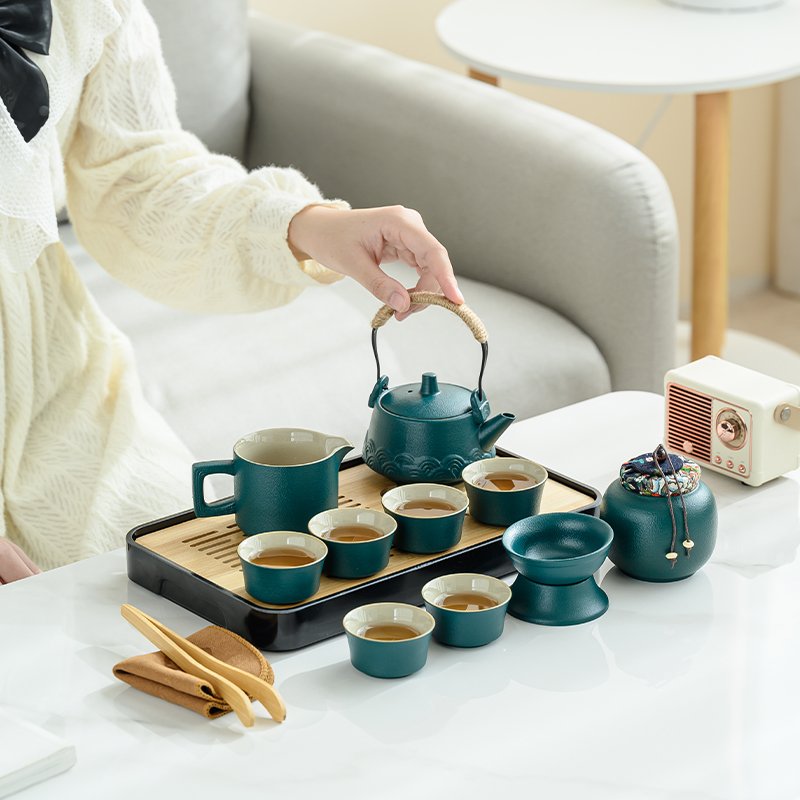 Teal ceramic teapot, pitcher, cups and tea accessories arranged on and beside a bamboo tray