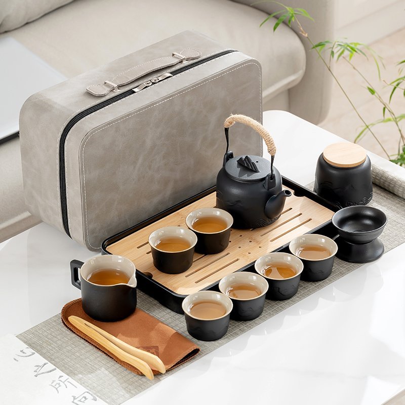Black ceramic travel tea set with six cups, an overhead-handle teapot, a tea tray and a gray carrying case