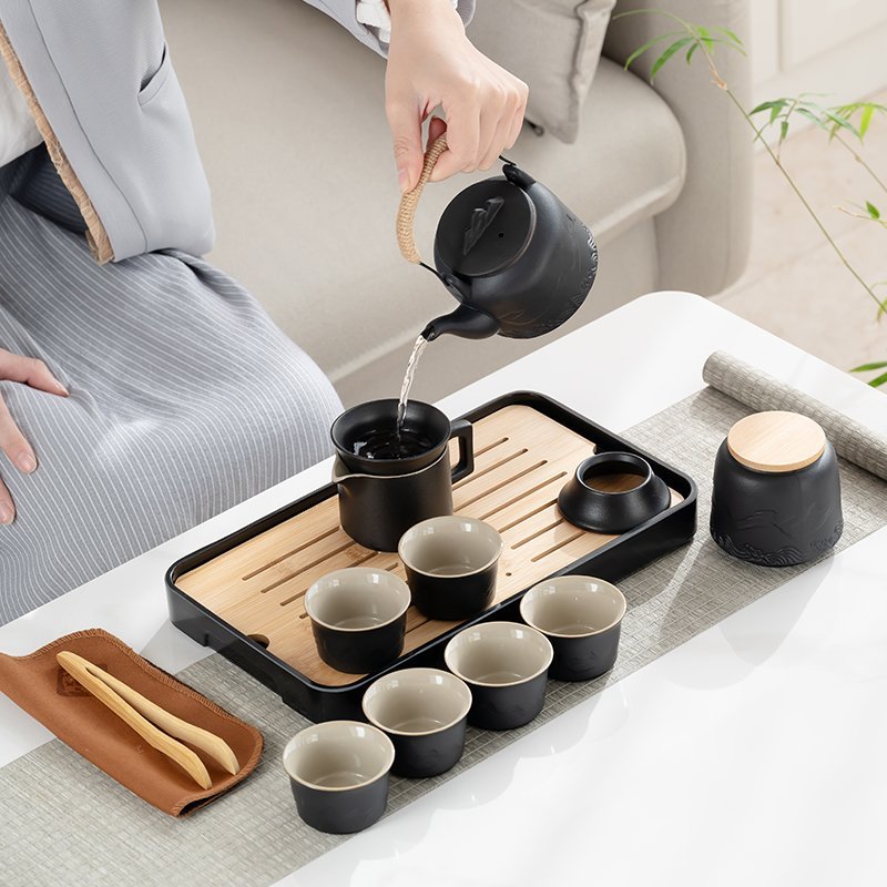 Overhead-handle teapot pouring through a tea strainer into the fairness pitcher beside six cups